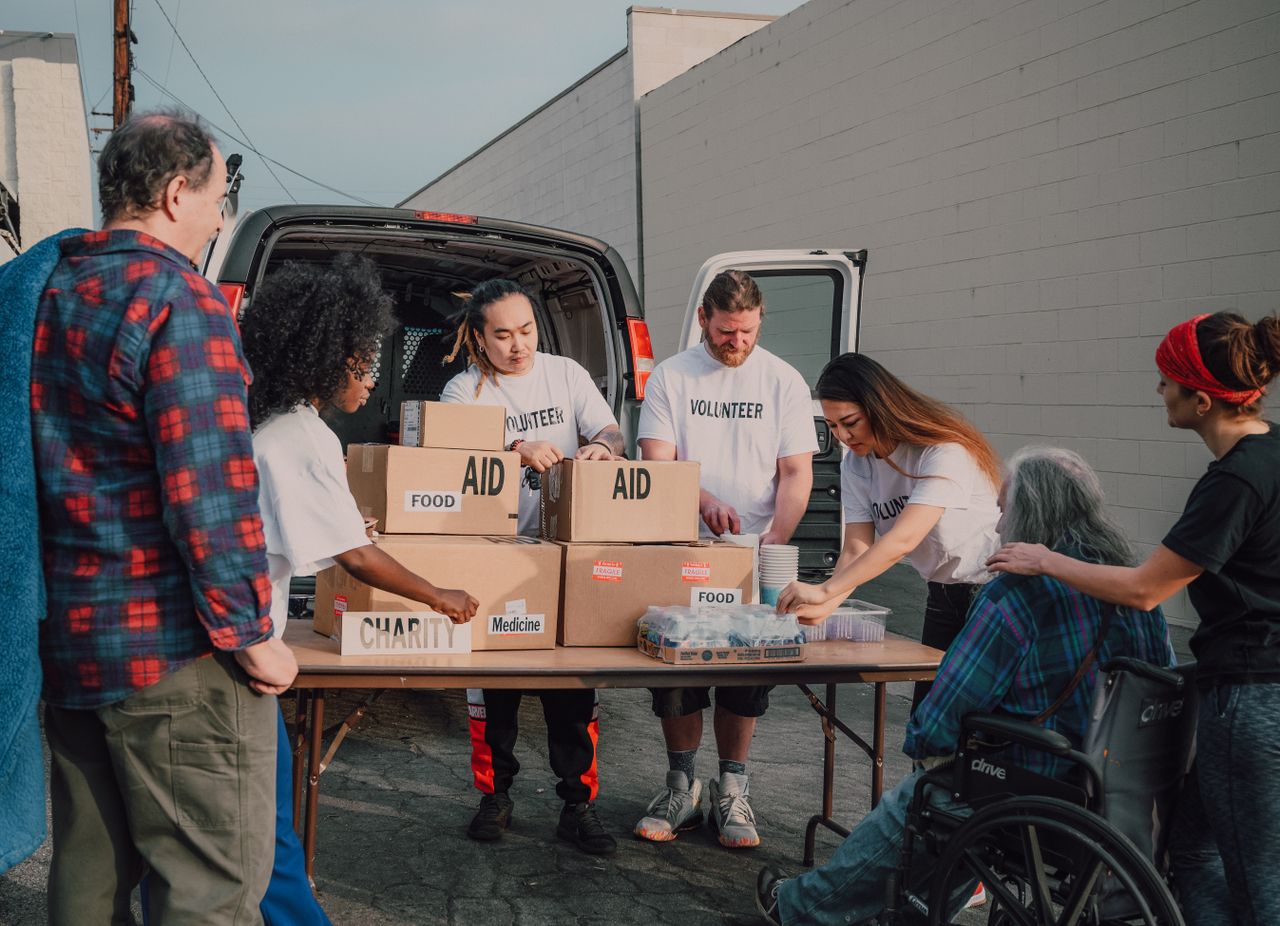 hero-img-02 Group of diverse volunteers organizing aid packages outdoors for a charity event.