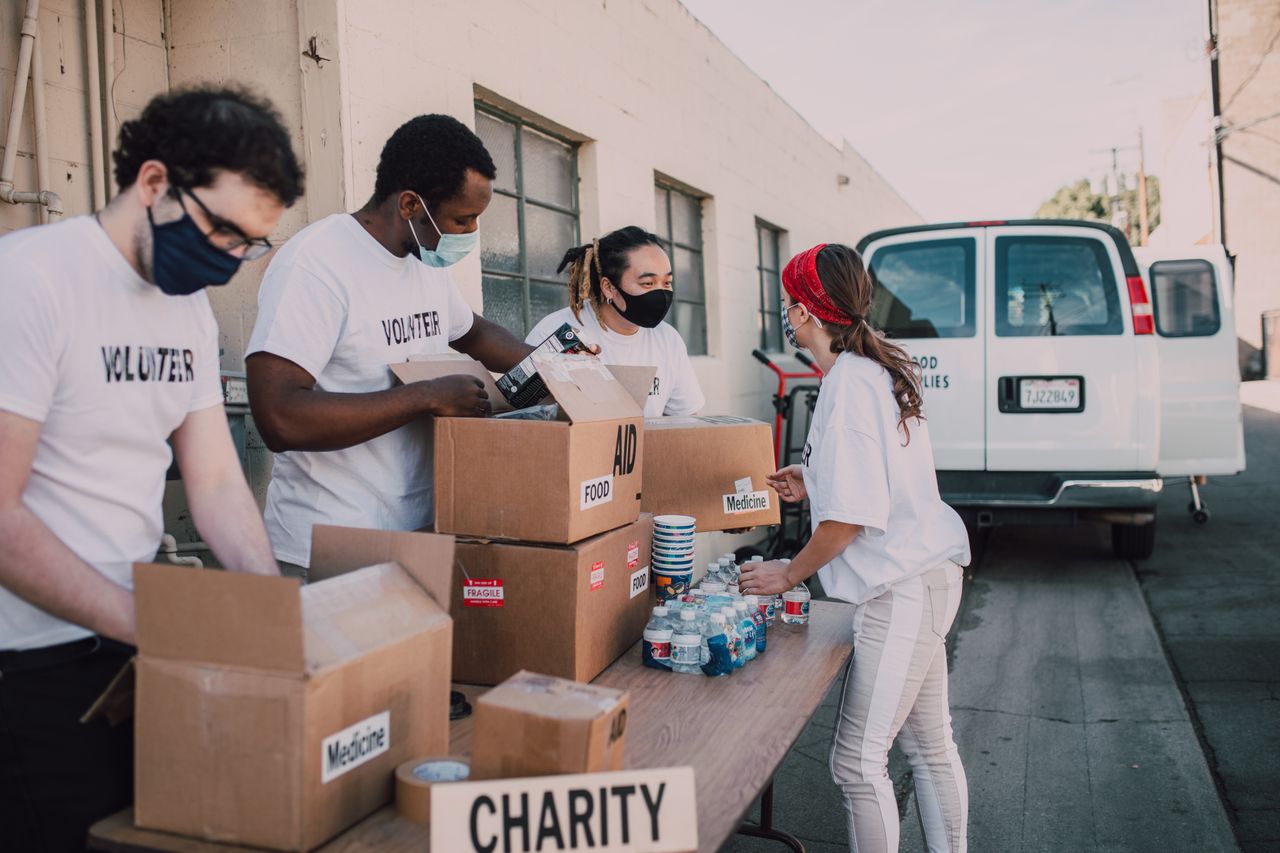 services-02 Group of volunteers wearing masks packing charity boxes outdoors during the pandemic.